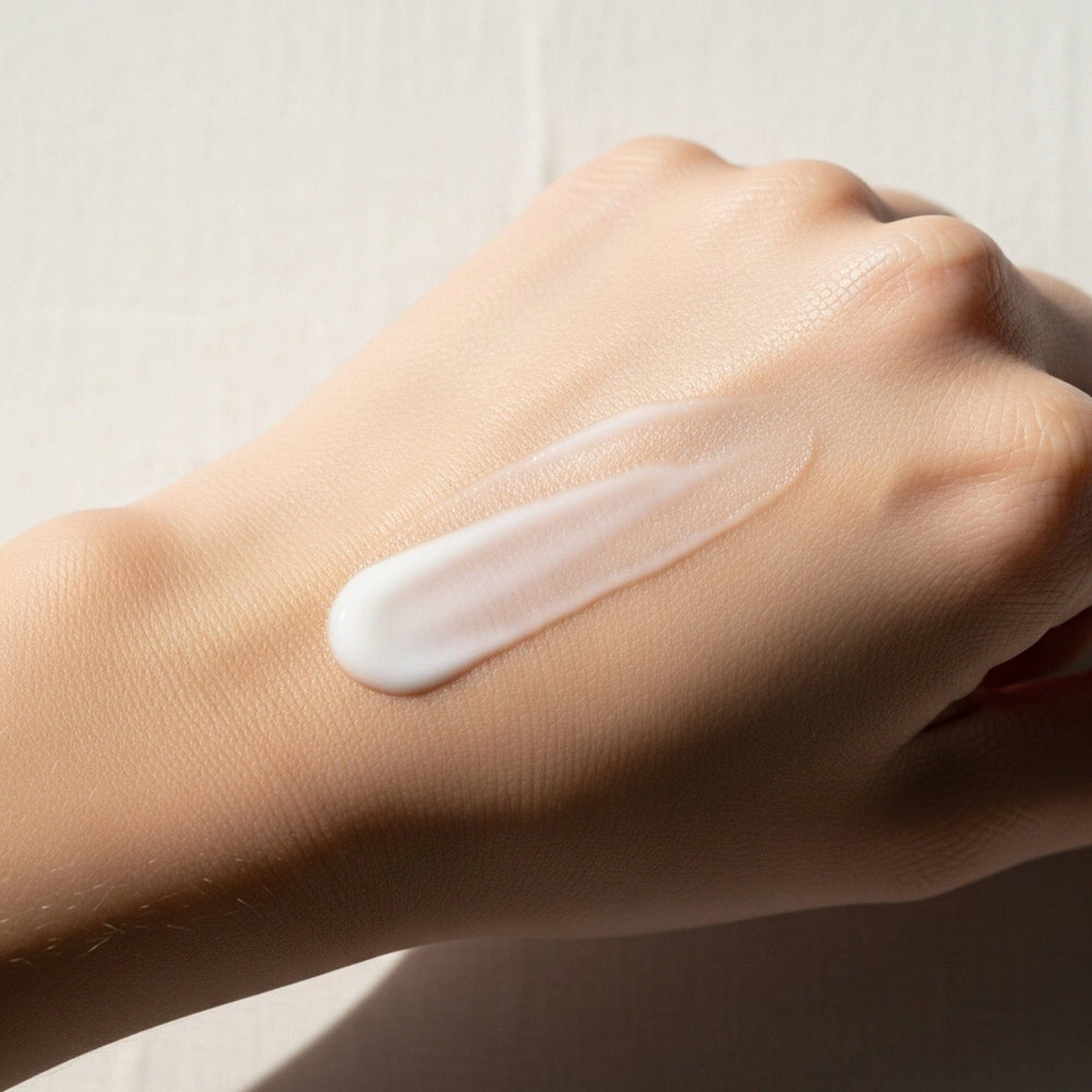 Hand with a swatch of cream on the wrist against a neutral background.