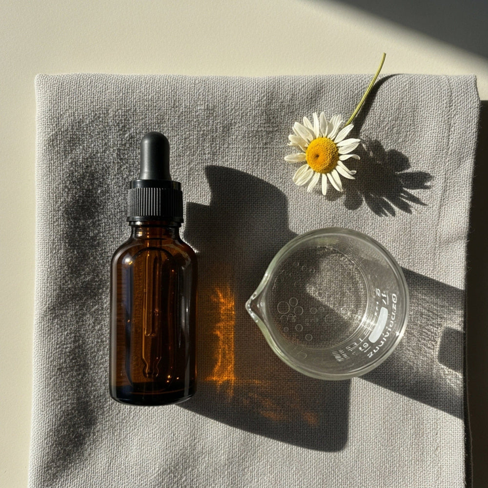 Brown glass dropper bottle with a white flower on a gray fabric background.
