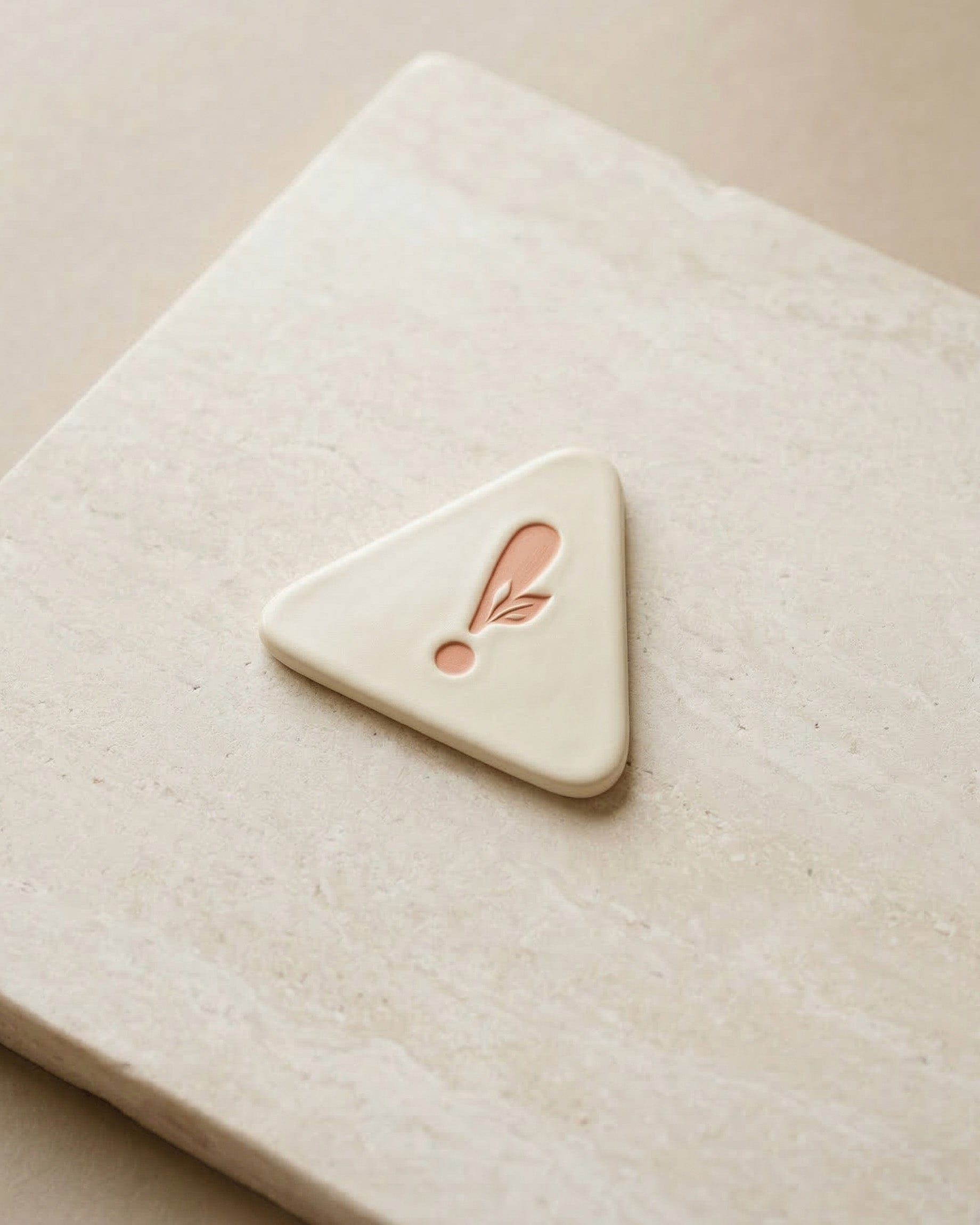 Triangular ceramic object with a pink feather design on a beige surface.
